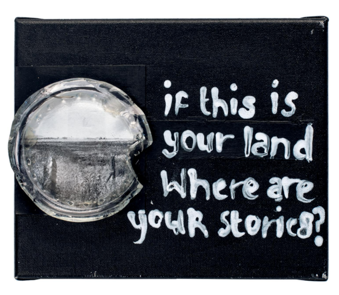 A work by the artist where, on black canvas, is written "If this is your land, where are your stories?" with a black and white picture of a landscape.